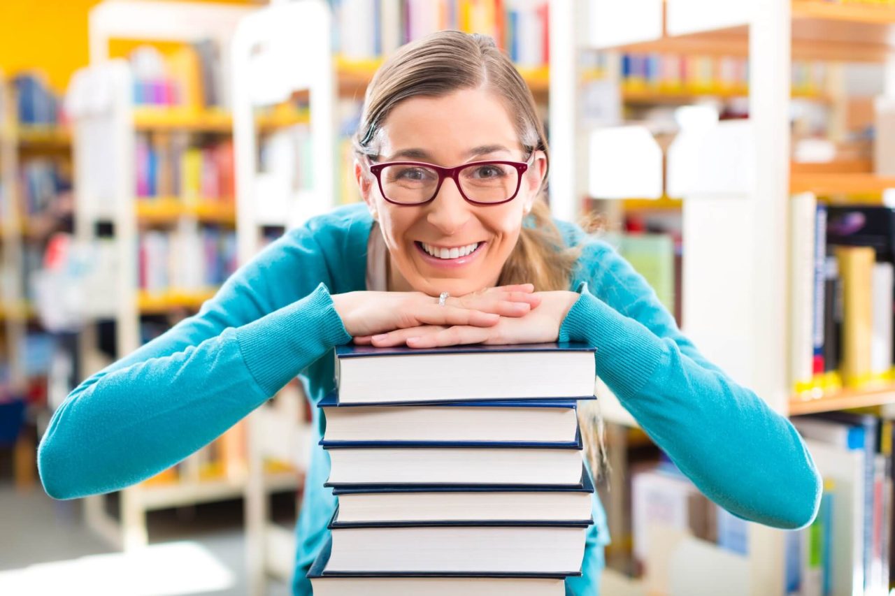 Ung kvinde smiler og har hagen på en stak bøger foran sig