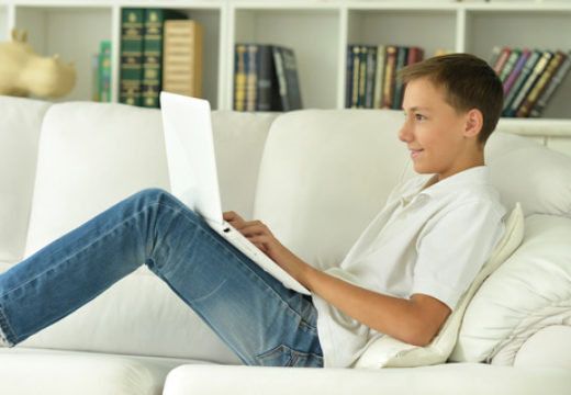 Ung mand sidder i sofaen hjemme med sin computer
